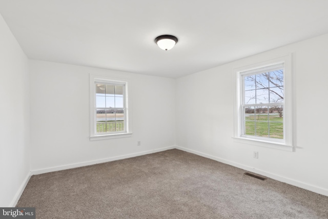 carpeted empty room featuring plenty of natural light, baseboards, and visible vents