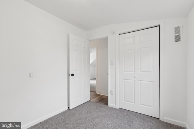 unfurnished bedroom with a closet, visible vents, baseboards, lofted ceiling, and carpet floors