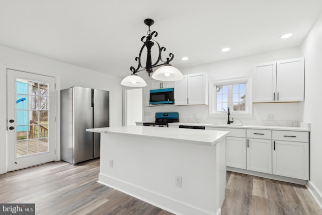 kitchen featuring light wood finished floors, a kitchen island, appliances with stainless steel finishes, a sink, and pendant lighting