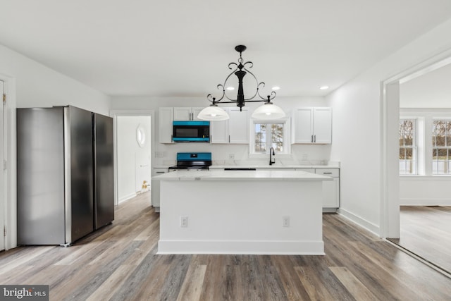 kitchen with light countertops, stainless steel appliances, a center island, light wood-style floors, and pendant lighting