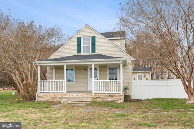 view of front of house with a shingled roof, a front yard, covered porch, and fence
