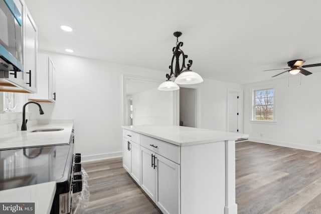 kitchen featuring a ceiling fan, white cabinetry, a sink, light wood-type flooring, and a center island