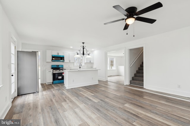 unfurnished living room featuring baseboards, light wood-style flooring, stairway, and ceiling fan with notable chandelier