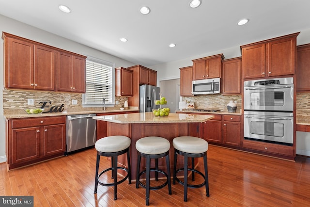 42694 Chisholm, Broadlands, VA 20148 - kitchen featuring stainless steel appliances, a kitchen island, a breakfast bar area, wood finished floors, and decorative backsplash