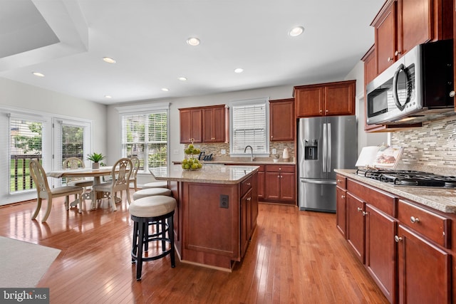 42694 Chisholm, Broadlands, VA 20148 - kitchen featuring appliances with stainless steel finishes, a kitchen bar, tasteful backsplash, light wood-style flooring, and a kitchen island