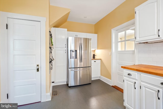 kitchen with tasteful backsplash, visible vents, stainless steel fridge, white cabinets, and baseboards