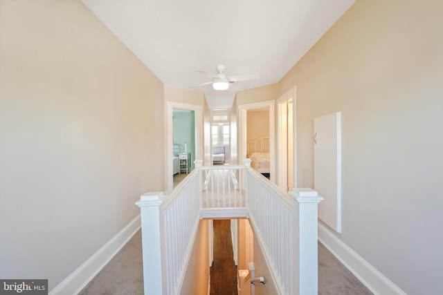 hallway featuring an upstairs landing, baseboards, and carpet floors