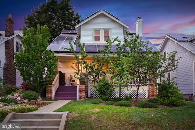 view of front of home featuring a front yard, brick siding, solar panels, and metal roof