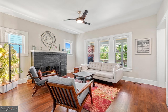 living room with a ceiling fan, a brick fireplace, visible vents, baseboards, and hardwood / wood-style flooring
