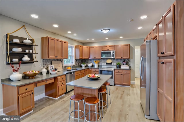 kitchen featuring appliances with stainless steel finishes, a sink, light wood-style floors, a kitchen breakfast bar, and recessed lighting