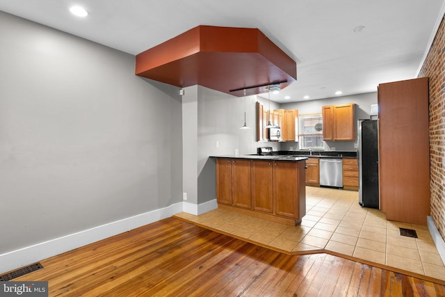 kitchen with baseboards, dark countertops, a peninsula, light wood-style floors, and stainless steel appliances