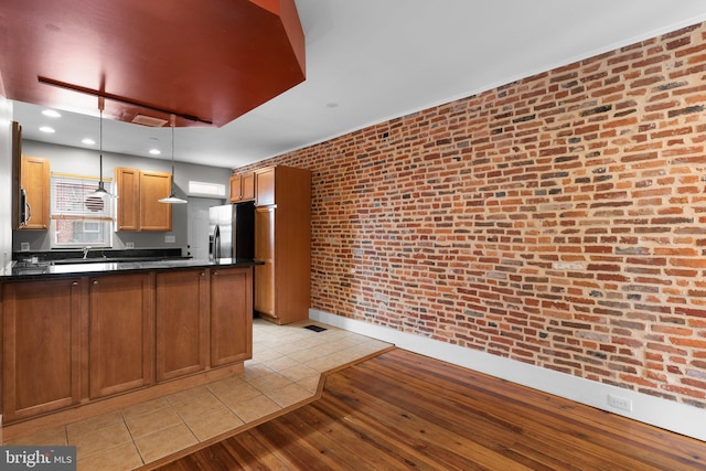 kitchen featuring light wood-style flooring, a peninsula, dark countertops, hanging light fixtures, and stainless steel appliances