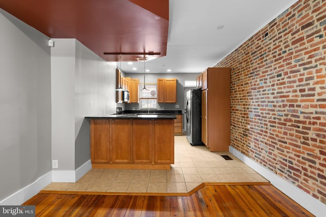 kitchen with light wood-type flooring, baseboards, brick wall, a peninsula, and stainless steel appliances