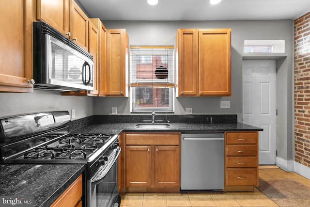 kitchen with dark stone counters, appliances with stainless steel finishes, light tile patterned floors, and a sink