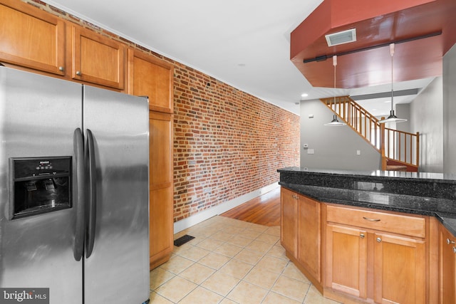 kitchen with dark stone countertops, light tile patterned floors, brick wall, stainless steel refrigerator with ice dispenser, and visible vents