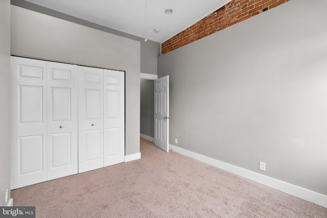 unfurnished bedroom with brick wall, baseboards, carpet floors, and a closet