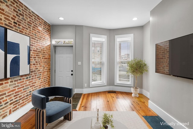 living area featuring recessed lighting, hardwood / wood-style flooring, baseboards, and brick wall
