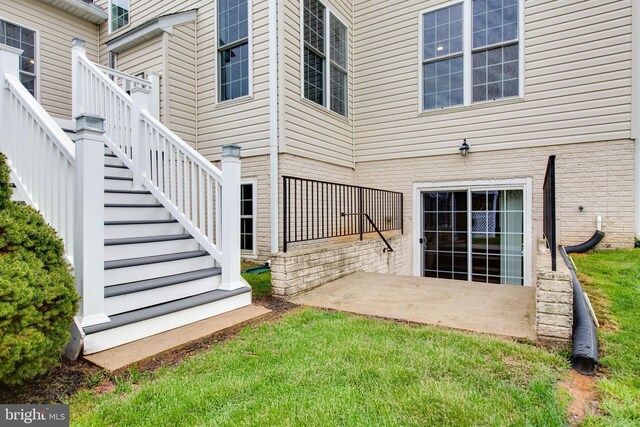 view of exterior entry with a lawn, brick siding, and a patio area