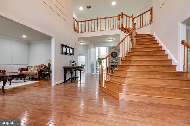 foyer entrance with visible vents, light wood-type flooring, stairway, baseboards, and a high ceiling