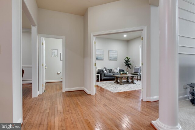 foyer entrance featuring light wood-type flooring, baseboards, and ornate columns