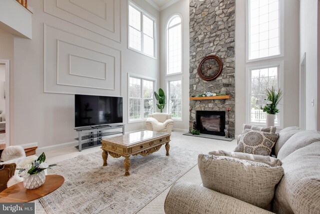 carpeted living room with a stone fireplace, baseboards, crown molding, and a high ceiling