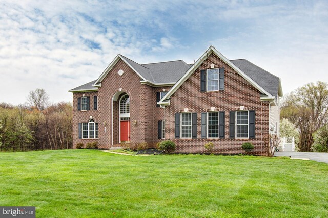view of front facade with brick siding, roof with shingles, and a front yard