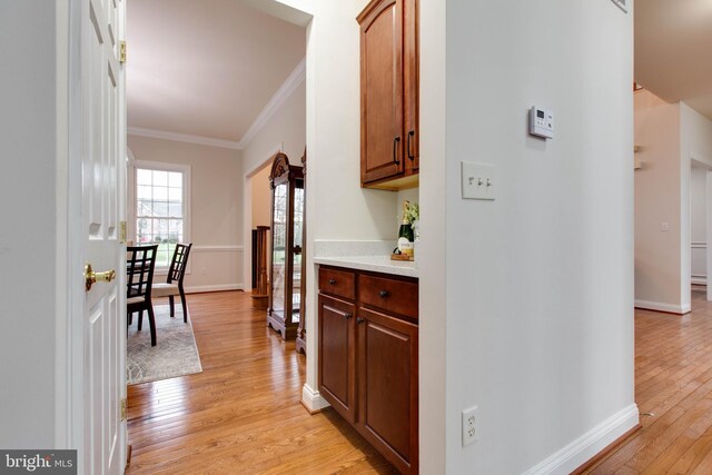 corridor featuring crown molding, baseboards, and light wood-style floors