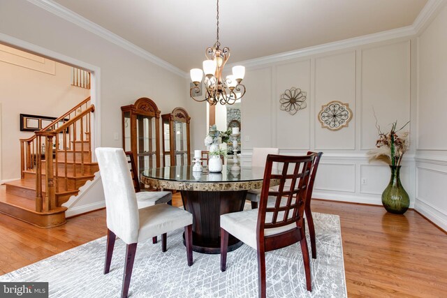 dining room with a decorative wall, an inviting chandelier, ornamental molding, and light wood-style floors