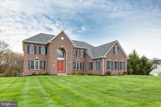 view of front of home with brick siding, central AC unit, a shingled roof, and a front yard