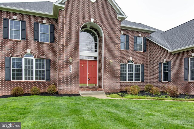 exterior space with roof with shingles, a front lawn, and brick siding