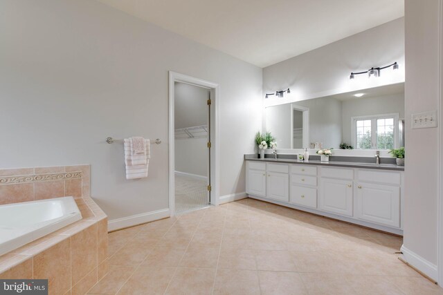 full bathroom with double vanity, a garden tub, a sink, tile patterned floors, and baseboards
