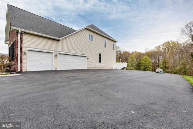view of property exterior featuring driveway, roof with shingles, and a garage