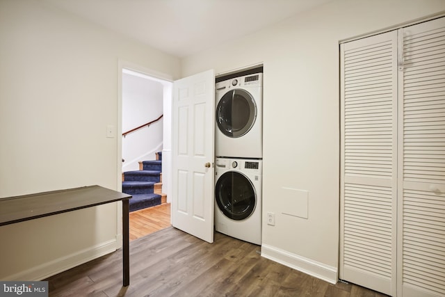 laundry room featuring estacked washer and dryer, wood finished floors, and baseboards