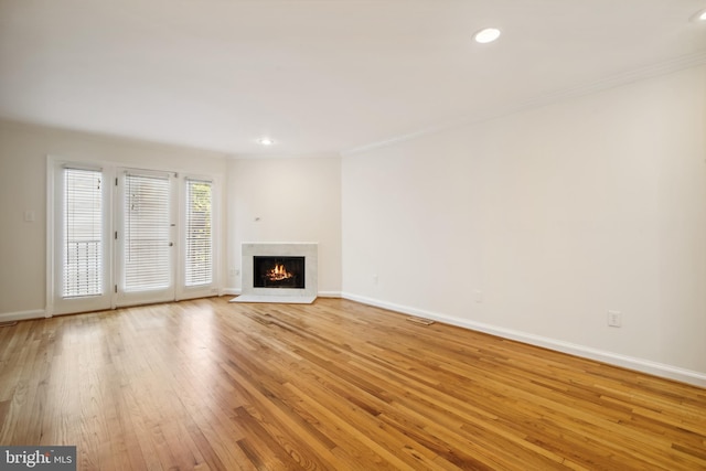 unfurnished living room with crown molding, a fireplace with flush hearth, light wood finished floors, baseboards, and recessed lighting