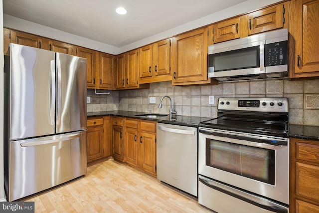kitchen featuring stainless steel appliances, a sink, brown cabinetry, and tasteful backsplash