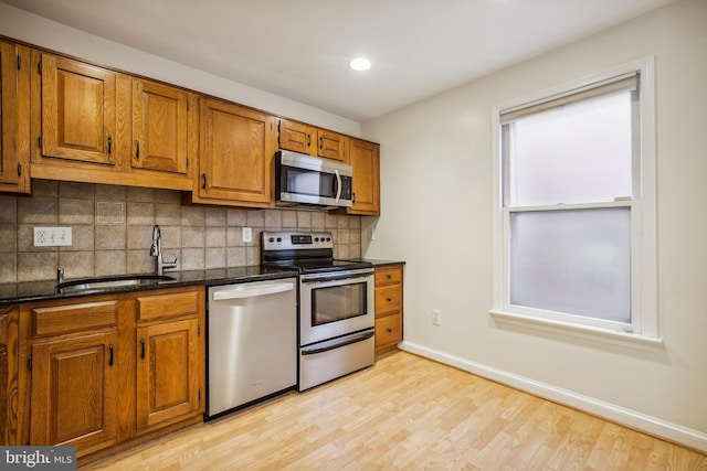 kitchen with appliances with stainless steel finishes, a sink, brown cabinets, tasteful backsplash, and light wood-style flooring