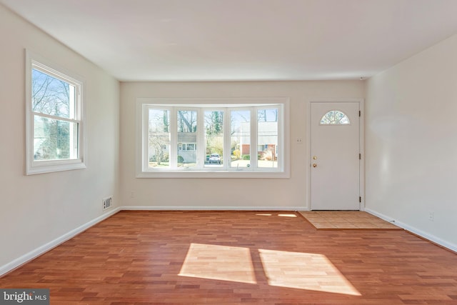 foyer entrance featuring baseboards, visible vents, and wood finished floors