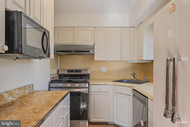 kitchen with light countertops, tasteful backsplash, under cabinet range hood, a sink, and appliances with stainless steel finishes