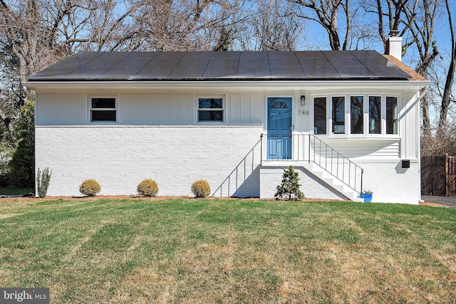 view of front facade with a chimney, roof mounted solar panels, brick siding, and a front yard