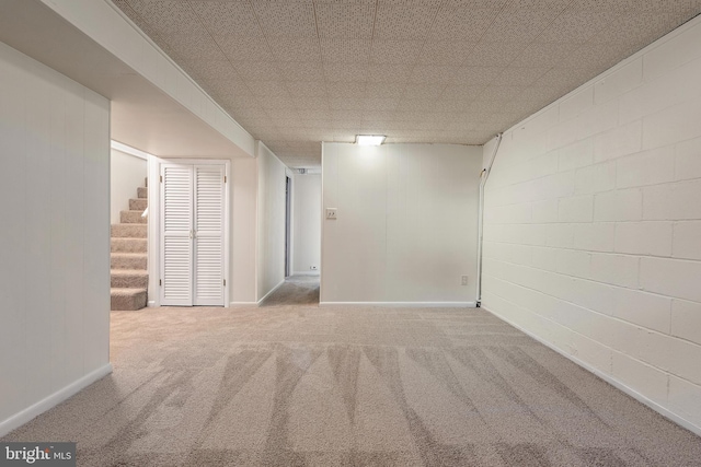 finished basement with stairs, concrete block wall, baseboards, and carpet flooring