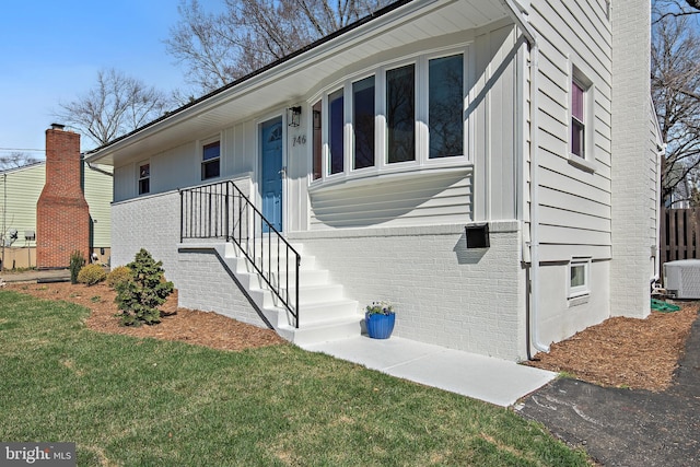 view of front of home with brick siding, a front yard, and central AC unit
