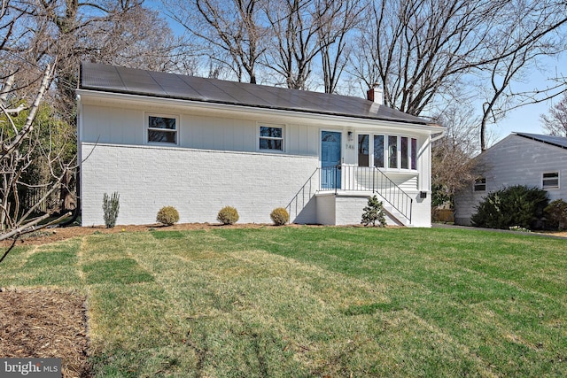 view of front of home featuring a chimney, brick siding, solar panels, and a front lawn