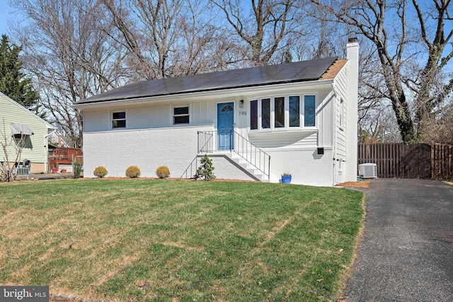 view of front of house with fence, a front lawn, brick siding, solar panels, and a chimney