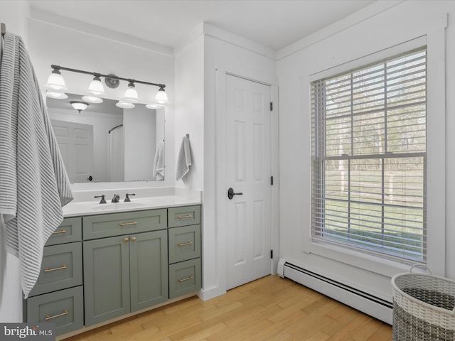 bathroom featuring wood finished floors, a healthy amount of sunlight, vanity, and baseboard heating