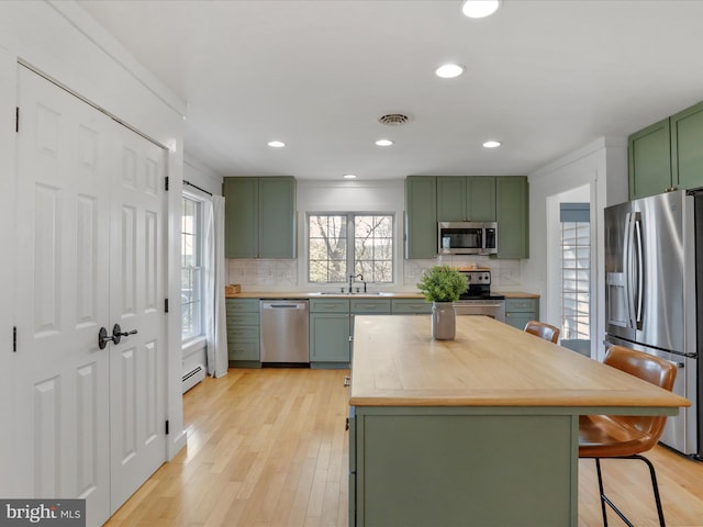 kitchen featuring baseboard heating, decorative backsplash, green cabinetry, and appliances with stainless steel finishes