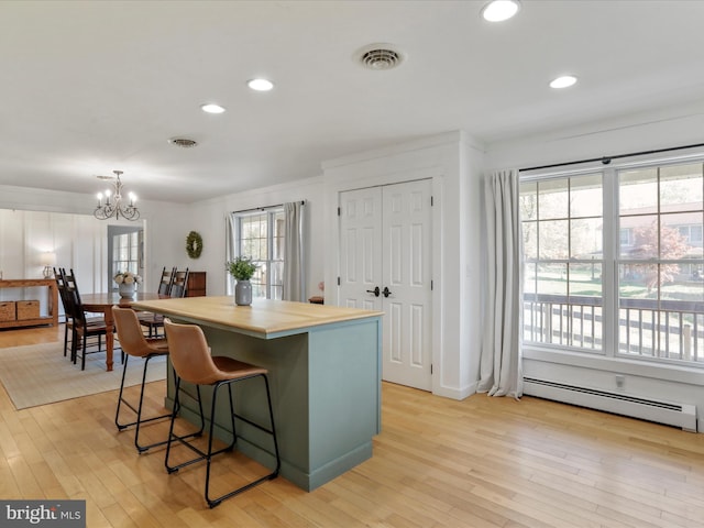 kitchen featuring a chandelier, visible vents, light wood-style floors, a center island, and a baseboard radiator