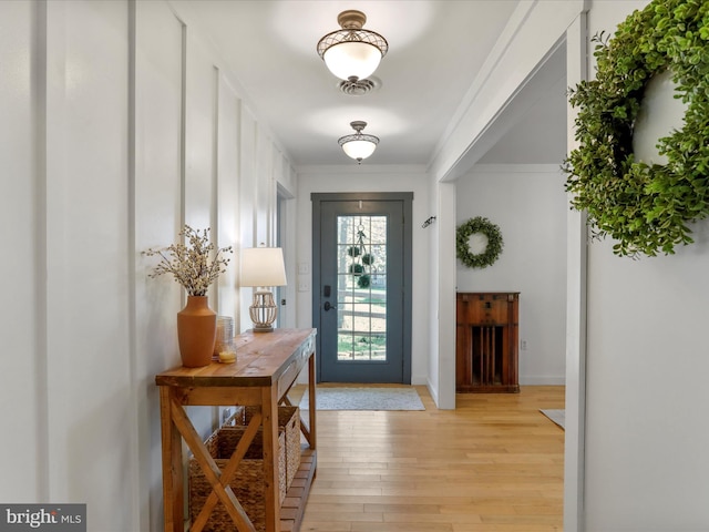 doorway featuring baseboards, crown molding, and light wood-style flooring