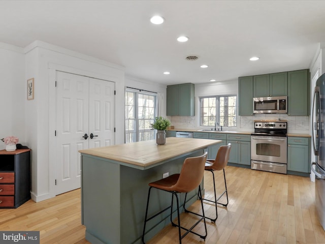 kitchen with light wood finished floors, green cabinets, and appliances with stainless steel finishes
