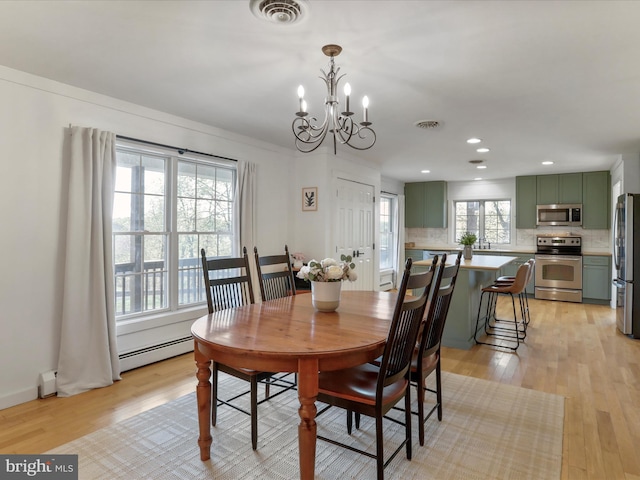 dining space featuring light wood-type flooring, visible vents, a notable chandelier, and a baseboard radiator