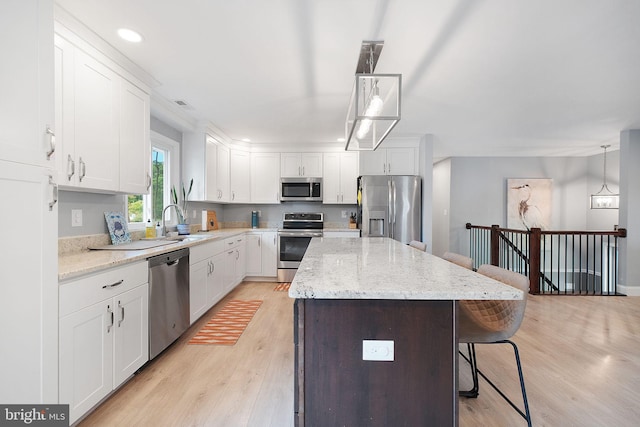 kitchen with appliances with stainless steel finishes, a sink, a breakfast bar area, a kitchen island, and light wood-type flooring